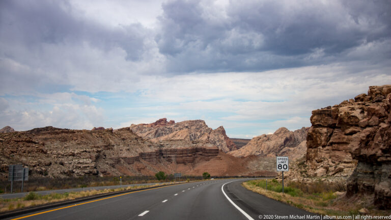 A highway curves into a sandstone canyon past an 80-mile-per-hour speed limit sign.