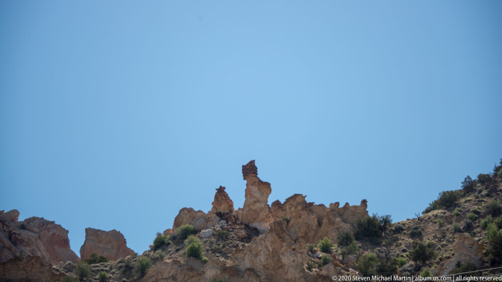 A tall central rock tower and smaller pinnacles rise above a red-and-cream ridge.