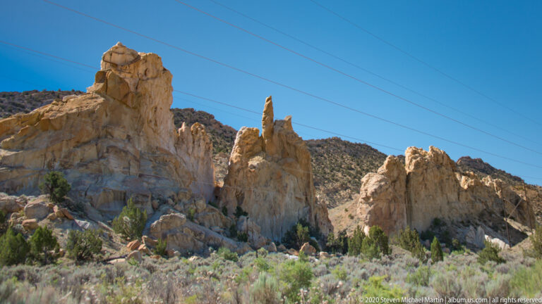 Pale and ochre sandstone fins rise above shrubs beneath several diagonal utility wires.