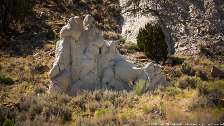 Rounded pale rock formations rise among sagebrush and juniper on a dark hillside.