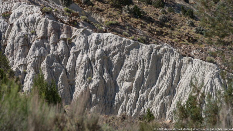 A broad white slope is etched with deep vertical ribs and narrow gullies.