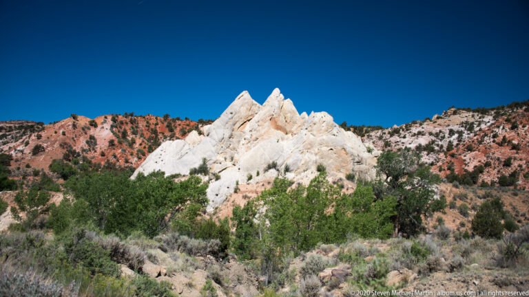 Pale pointed spires rise above juniper and sagebrush on a red-and-cream hillside.