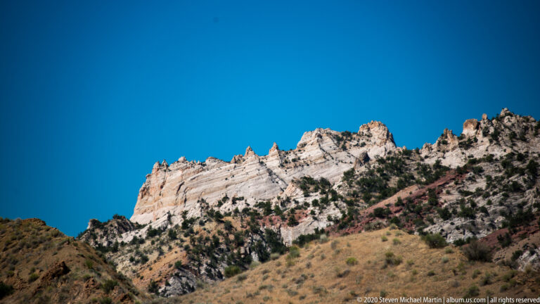 A bright white ridge with broken pinnacles stretches beneath a deep blue sky above tawny slopes.