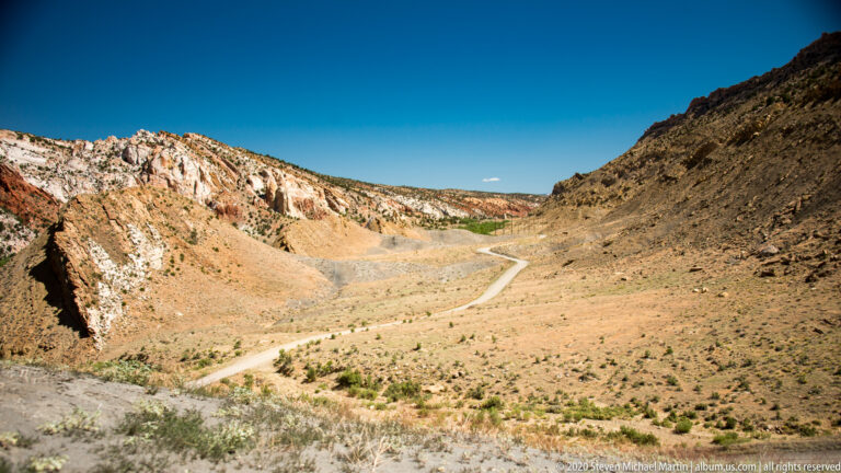 A light dirt route traverses the center of a dry basin beneath pale rock walls and darker hills.