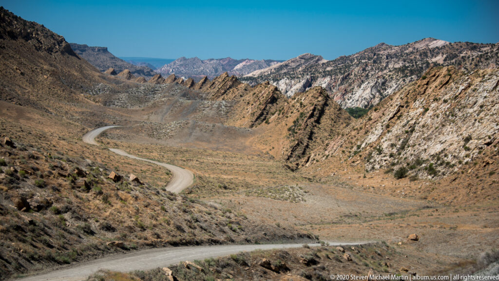 The road sweeps across the lower foreground and loops through a wide basin beneath layered mountains.