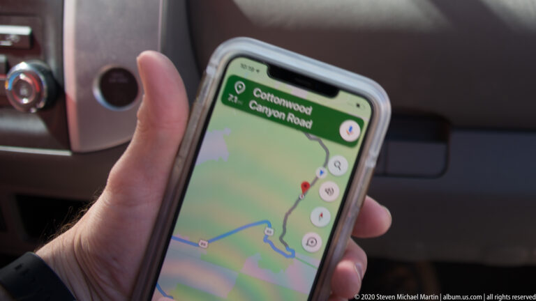 A hand holds a smartphone showing a map and route for Cottonwood Canyon Road inside a vehicle.