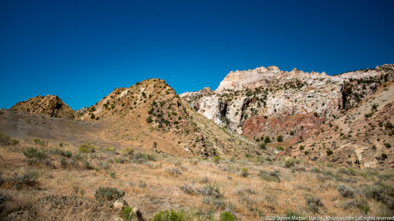 Tawny grassland fills the foreground below a low green-brown hill and pale horizontal rock bands.