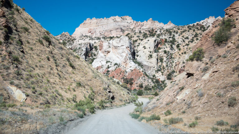The road occupies the foreground and narrows between light-colored slopes, with a darker opening in the right wall.