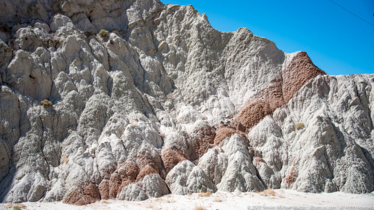 White and gray ridges form sharp gullies, with a red diagonal layer cutting through the upper slope.