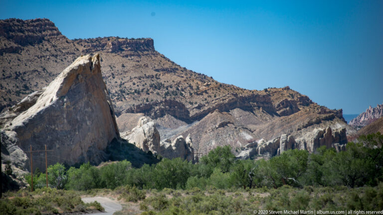 A dark pointed formation at left overlooks white pinnacles, scrub, and layered brown hills.
