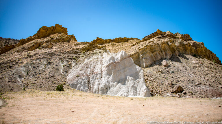 A bright white band crosses the lower slope beneath tan and gray hills with a jagged upper edge.