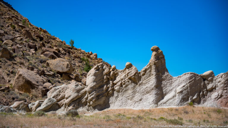 Cream-colored ridges form a serrated line beneath a slender capped spire and blue sky.