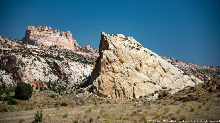A slanted cream rock face rises in front of pale layered hills and darker scrub.