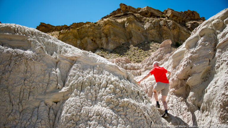 A person in a red shirt steps upward on the right side of a deeply grooved light-colored slope.