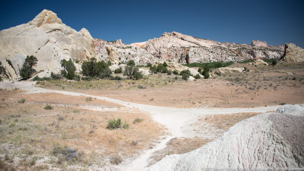 A chalky triangular rock occupies the lower right while a winding route crosses the valley toward pale ridges.