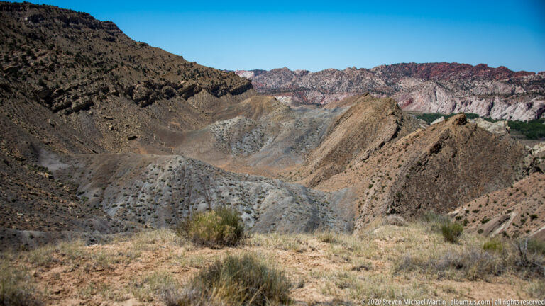 Gray, blue-green, and tan eroded slopes fill a basin between dark ridges.