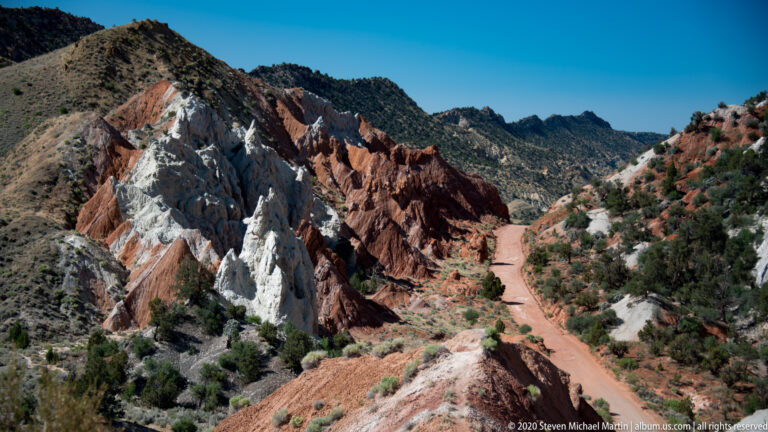 A dirt road winds through red and white rock walls toward darker hills.