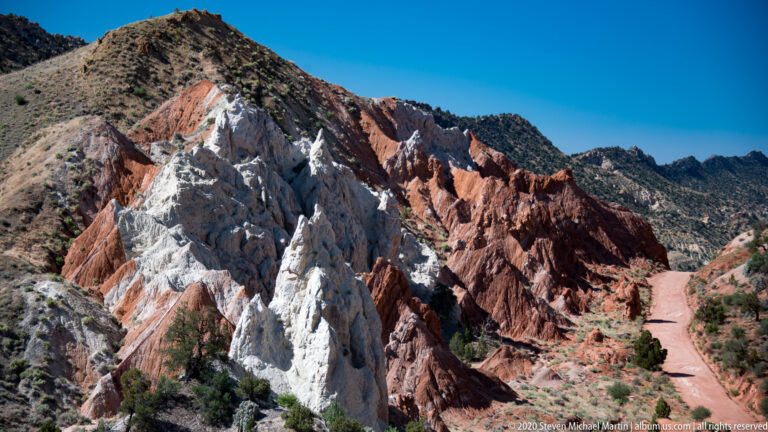 A narrow dirt track passes beside white, gray, and red sandstone fins.
