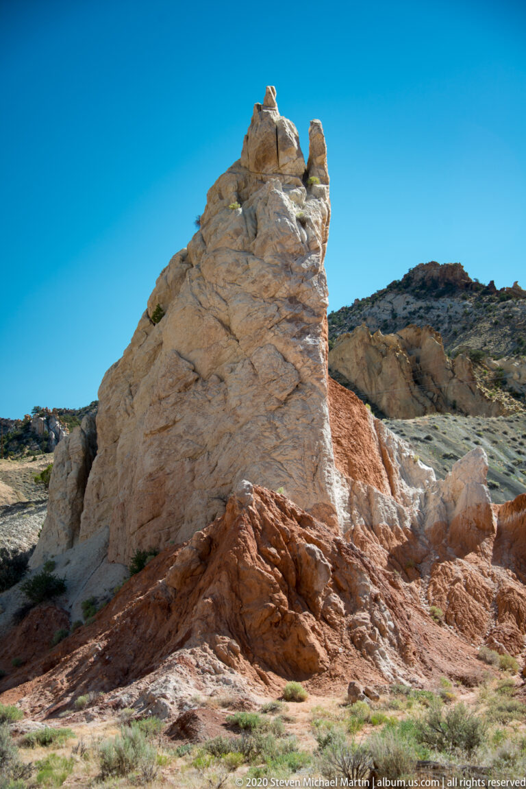 A broad pale sandstone tower rises from red rock above a gravelly basin.