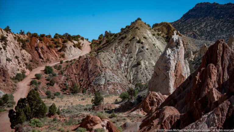 A pale ridgeline rises beyond a dirt road framed by red sandstone fins.