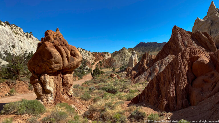 A rounded red capstone balances on a pale pedestal beside a steep sandstone ridge.