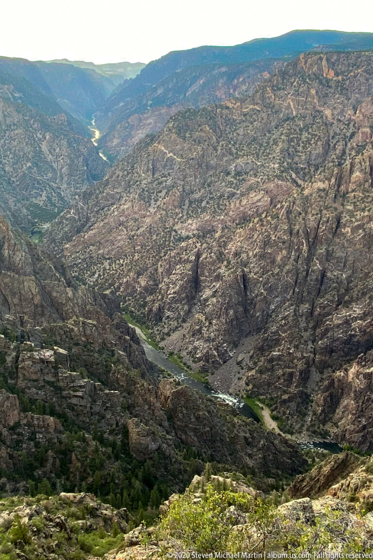A river winds through a broad rugged valley toward distant hills beneath a clear sky.