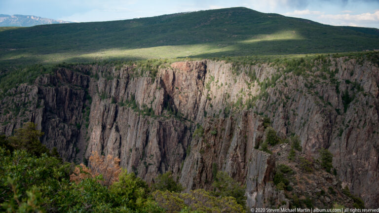 A forested plateau ends at a sheer cliff marked by vertical rock ribs.