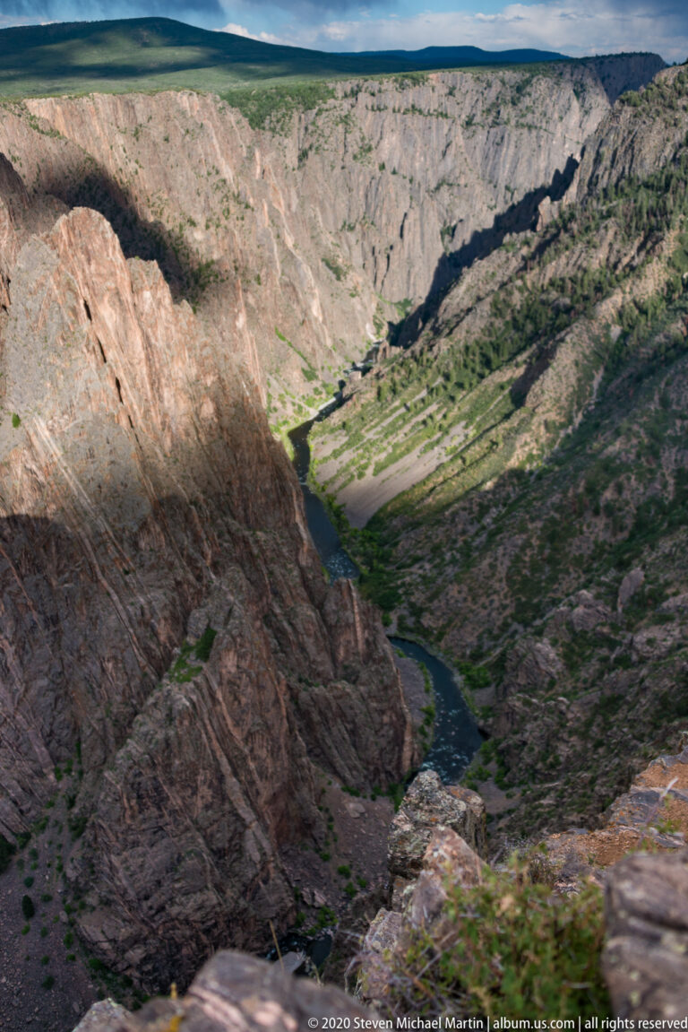 The river bends far below between a shadowed cliff and layered canyon slopes.