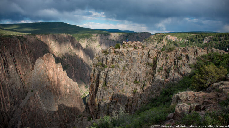 A clouded sky hangs over a broad gorge with sunlit sections of the far cliff.