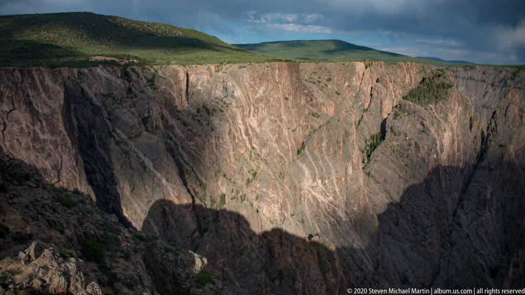 A sunlit canyon rim overlooks steep walls that descend into a deep shadowed gorge.