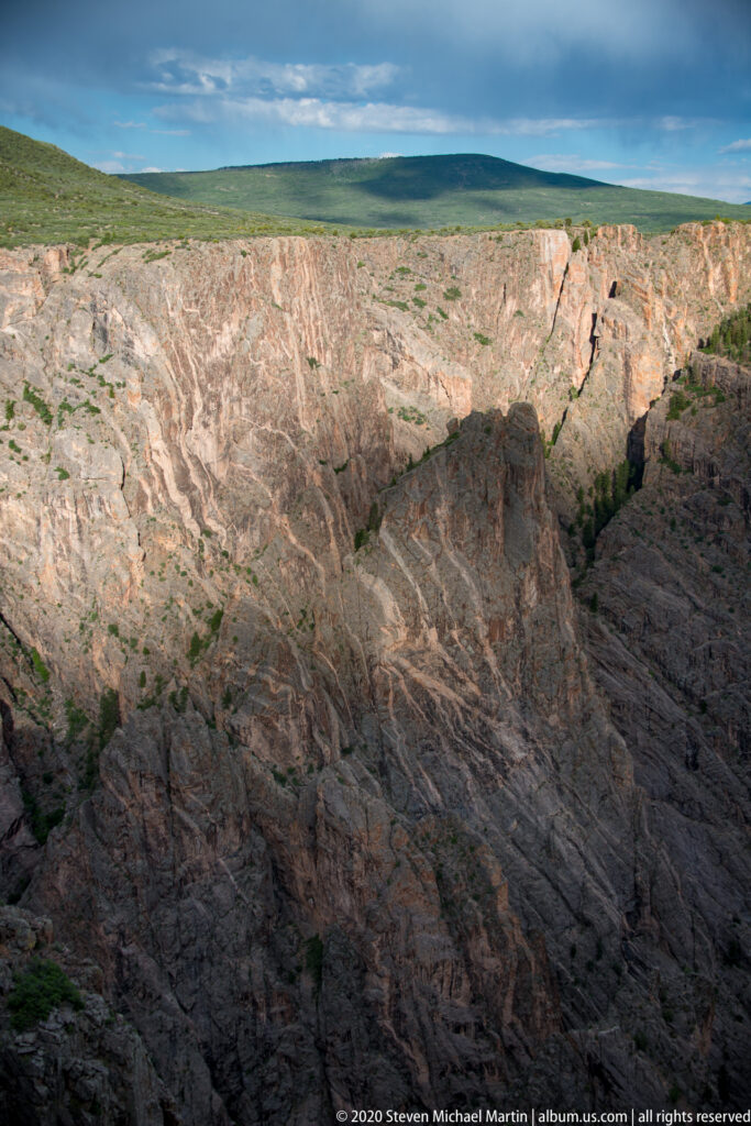 A broad canyon opens toward pale cliffs and a green plateau beneath a clouded sky.