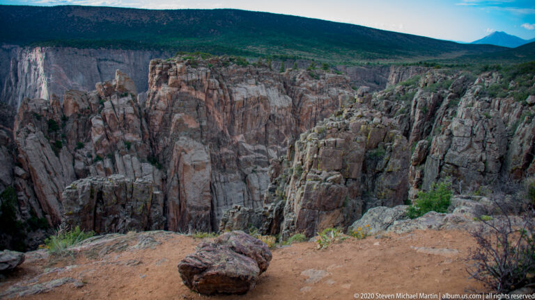 A rounded boulder sits at a canyon overlook above steep cliffs and a river far below.