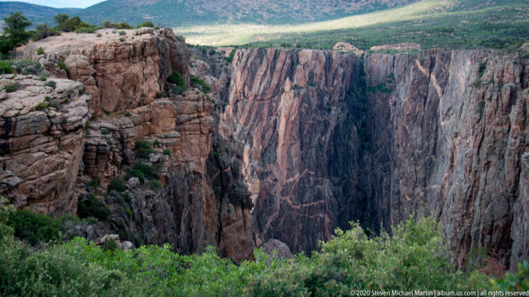 Sheer rock walls close around a narrow, shadowed gorge with sparse vegetation along the rim.