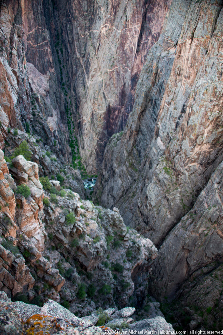 A narrow stream winds between boulders at the bottom of a steep, rocky canyon.