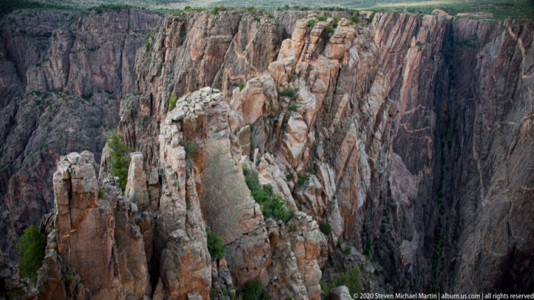 Fractured cliffs with pale mineral bands and scattered evergreen trees rise above the inner gorge.