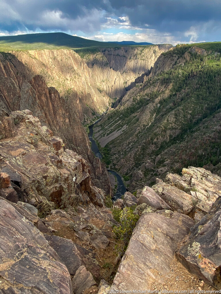 A broad rocky overlook frames the Gunnison River as it winds through a deep canyon.