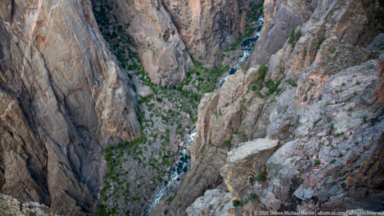 A narrow river threads through the bottom of a deep canyon between steep rock walls.