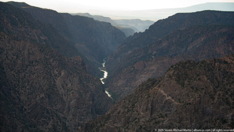 A winding river recedes through a hazy canyon between dark, layered mountain walls.