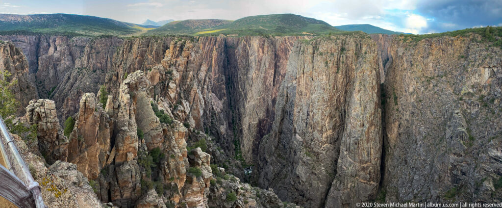 A grassy plateau borders a vast gorge with the Gunnison River visible between fractured cliffs.