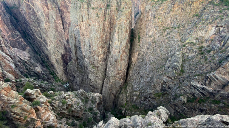 Jagged rocks at the rim overlook narrow clefts and ledges deep in the canyon.