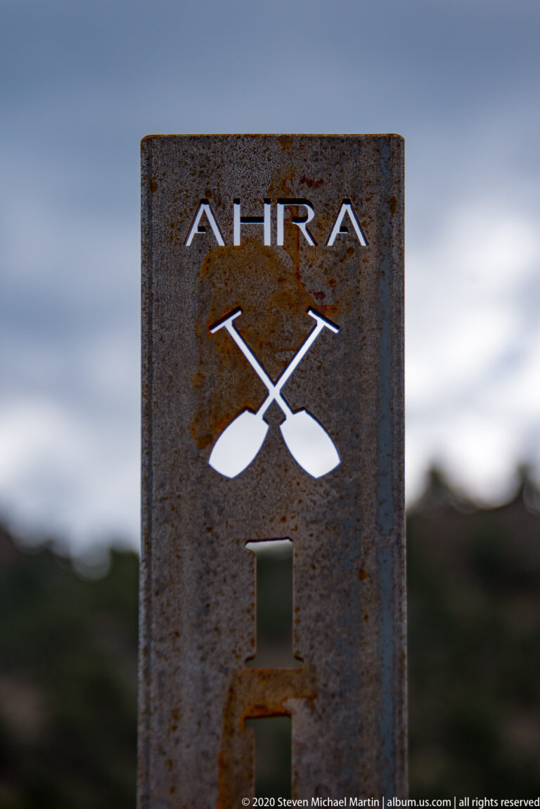 A weathered AHRA marker shows crossed paddles against a blurred valley background.