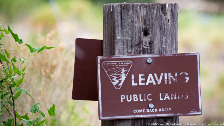 A brown “Leave No Trace” public-lands sign is mounted on a weathered post against softly blurred vegetation.