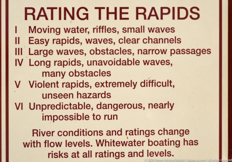 A close view of a boating sign explains whitewater classes I through VI and warns that river conditions change.