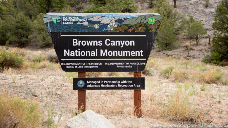 A Browns Canyon National Monument sign stands amid dry grasses and shrubs, identifying federal agency partners.