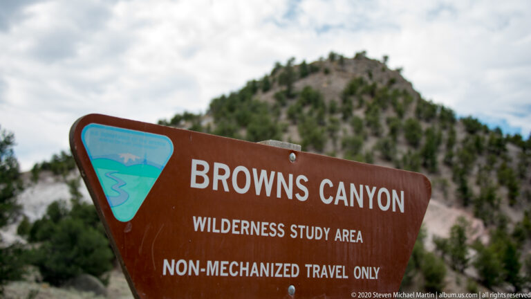 A brown Browns Canyon Wilderness Study Area sign states “Non-Mechanized Travel Only,” with a rocky hill blurred behind it.