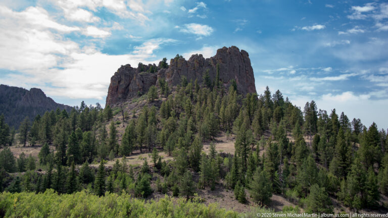 Fractured rocky summit above a conifer-covered slope beneath scattered clouds in Browns Canyon.