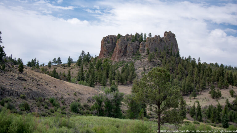 Distant rocky outcrop above a wooded hillside and green valley under a cloudy sky.