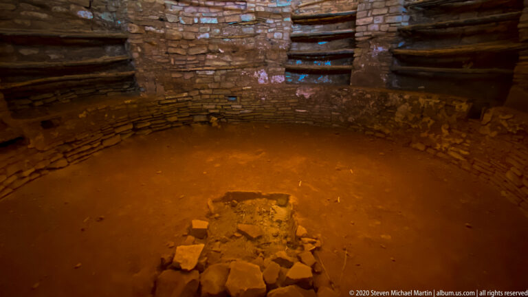 A circular stone chamber has a low central stone feature and beams near its upper wall.