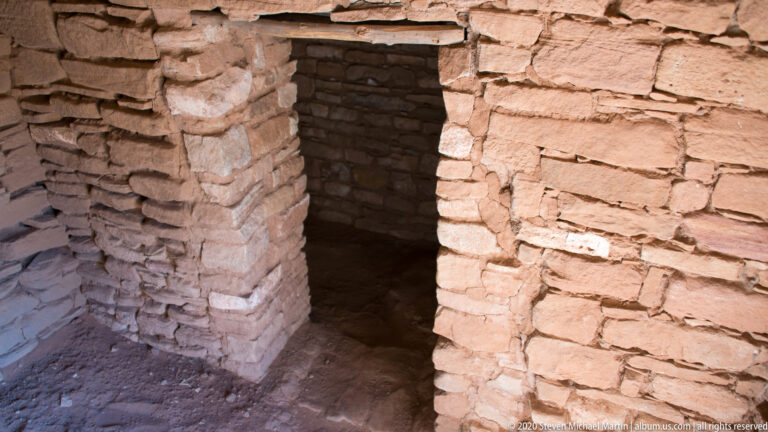 A narrow doorway in a thick stone wall opens into a dark interior.