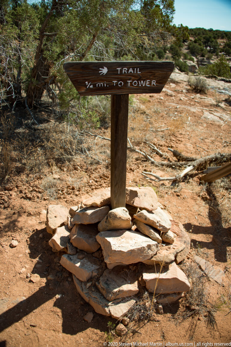 A wooden Trail to Tower sign with a left arrow stands above flat stones on a dry trail.
